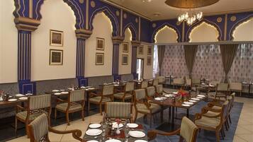 Un comedor formal con varias mesas y sillas, decoraciones ornamentales en azul y oro en las paredes, y un candelabro.