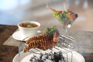 A grilled chicken on a wire rack over charcoal, a bowl of soup, and a glass salad with a toothpick.