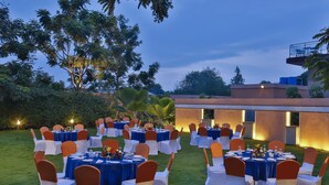 An outdoor dining area with round tables and chairs, surrounded by greenery and a building in the background. -  Mysore County Retreat (Mysore)