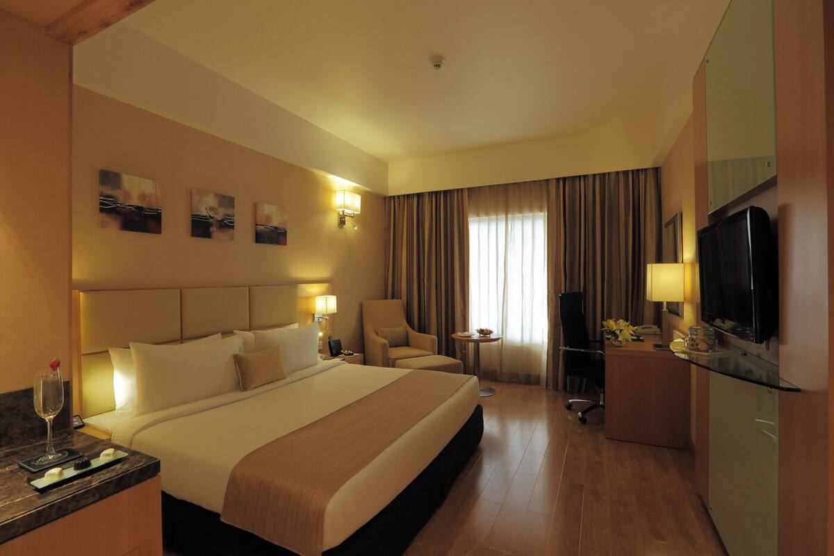 A hotel room with a large bed, a desk with a computer, a TV, and a chair.
