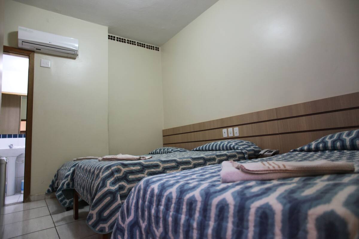 A hotel room with three beds, a bathroom, and an air conditioning unit.