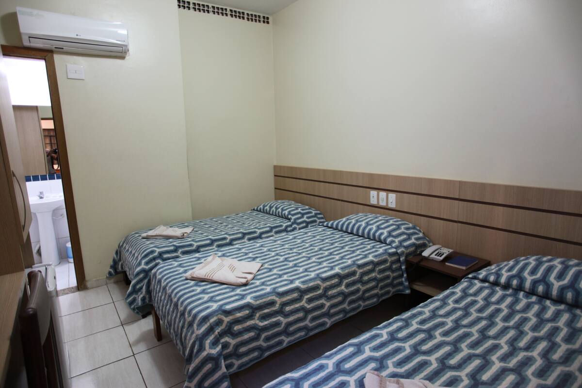 A hotel room with two beds, a wooden headboard, a bedside table with a phone, and an air conditioning unit on the wall.