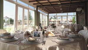 Un espace repas avec des tables dressées pour le repas, de grandes fenêtres et une vue sur l’extérieur.