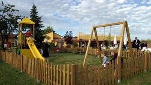 Une aire de jeux avec un toboggan jaune et des balançoires, entourée d’une clôture en bois.