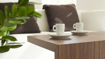 Una sala de estar moderna con una mesa de centro de madera, dos tazas blancas sobre platillos, una planta en maceta y un sofá marrón con un cojín oscuro.