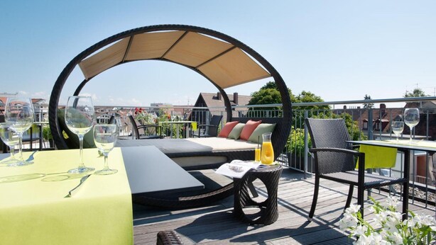 Een dakterras met een parasol, zitgedeelte, tafel met drankjes en uitzicht over de stad.