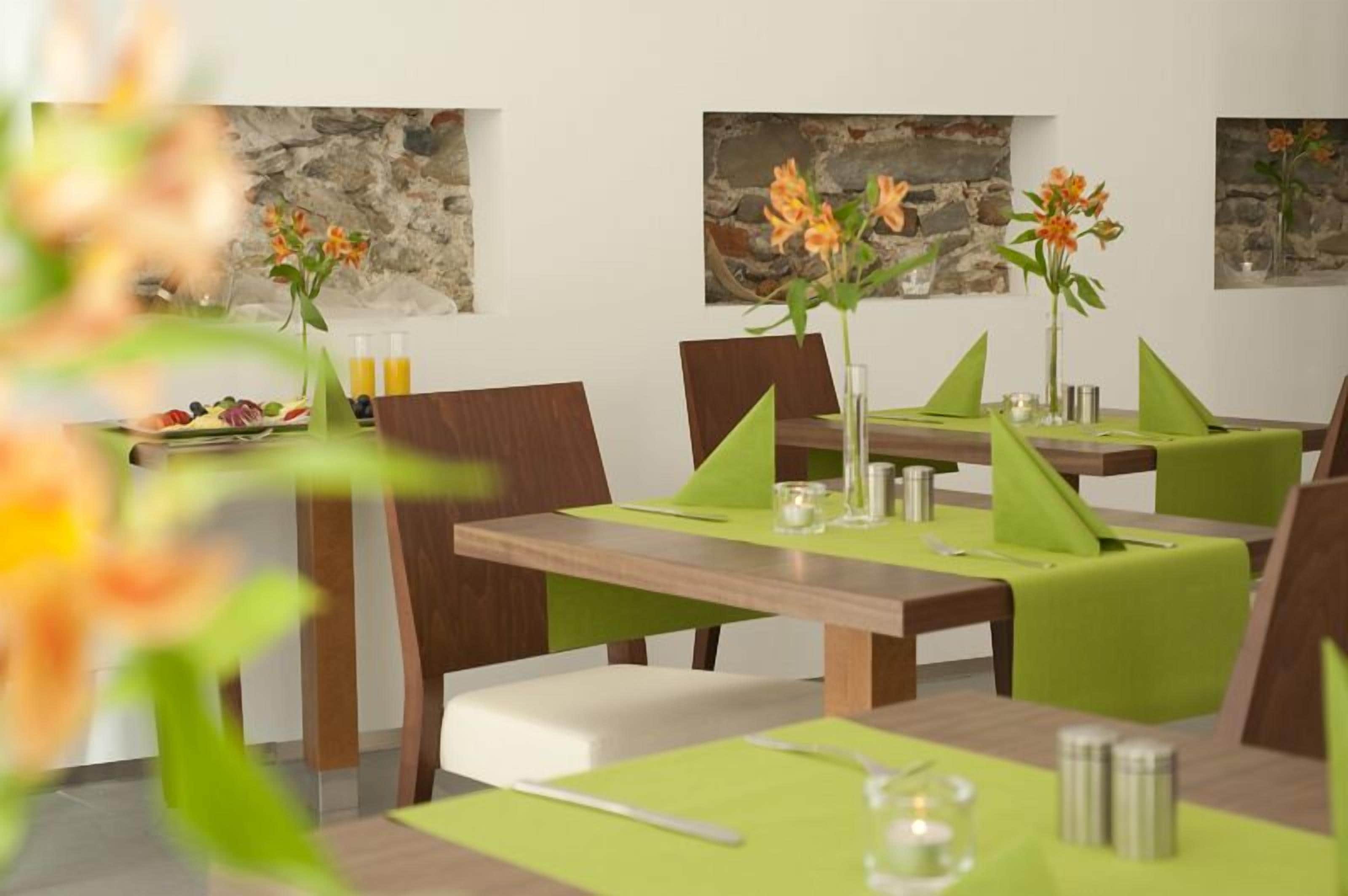 Ein moderner Essbereich mit Holztischen und grünen Sitzgelegenheiten, dekoriert mit orangefarbenen Blumen.