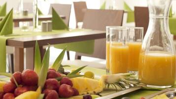 Una escena de desayuno con una bandeja de frutas, vasos de jugo y una jarra de zumo de naranja sobre una mesa.
