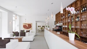 Een moderne bar met een lange toonbank, witte banken en een houten kastenwand met flessen en glazen.