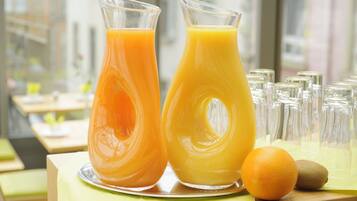Dos botellas de vidrio con jugo de naranja sobre una mesa con mantel verde, una naranja entera y un kiwi.