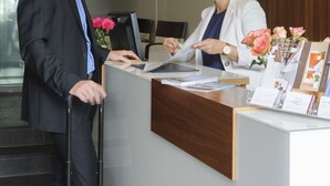 A reception desk with a wooden panel, a computer, and a vase with flowers. - Hotel Augustiner Tor (Konstanz)