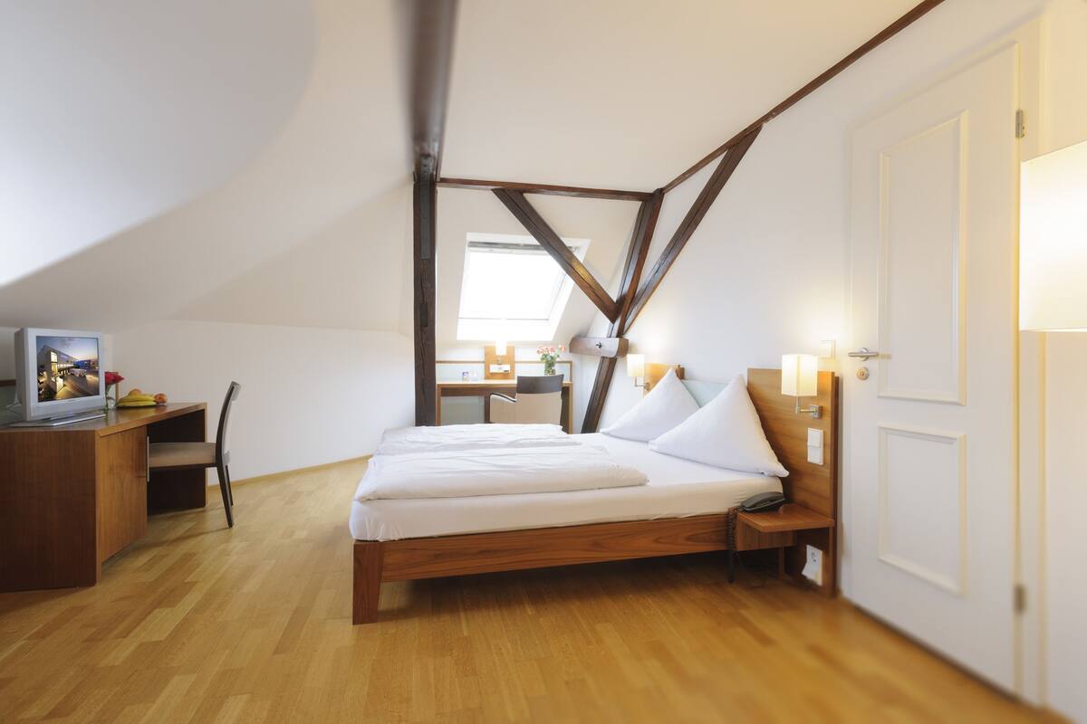 A bedroom with a wooden bed, a desk, a chair, and a TV.