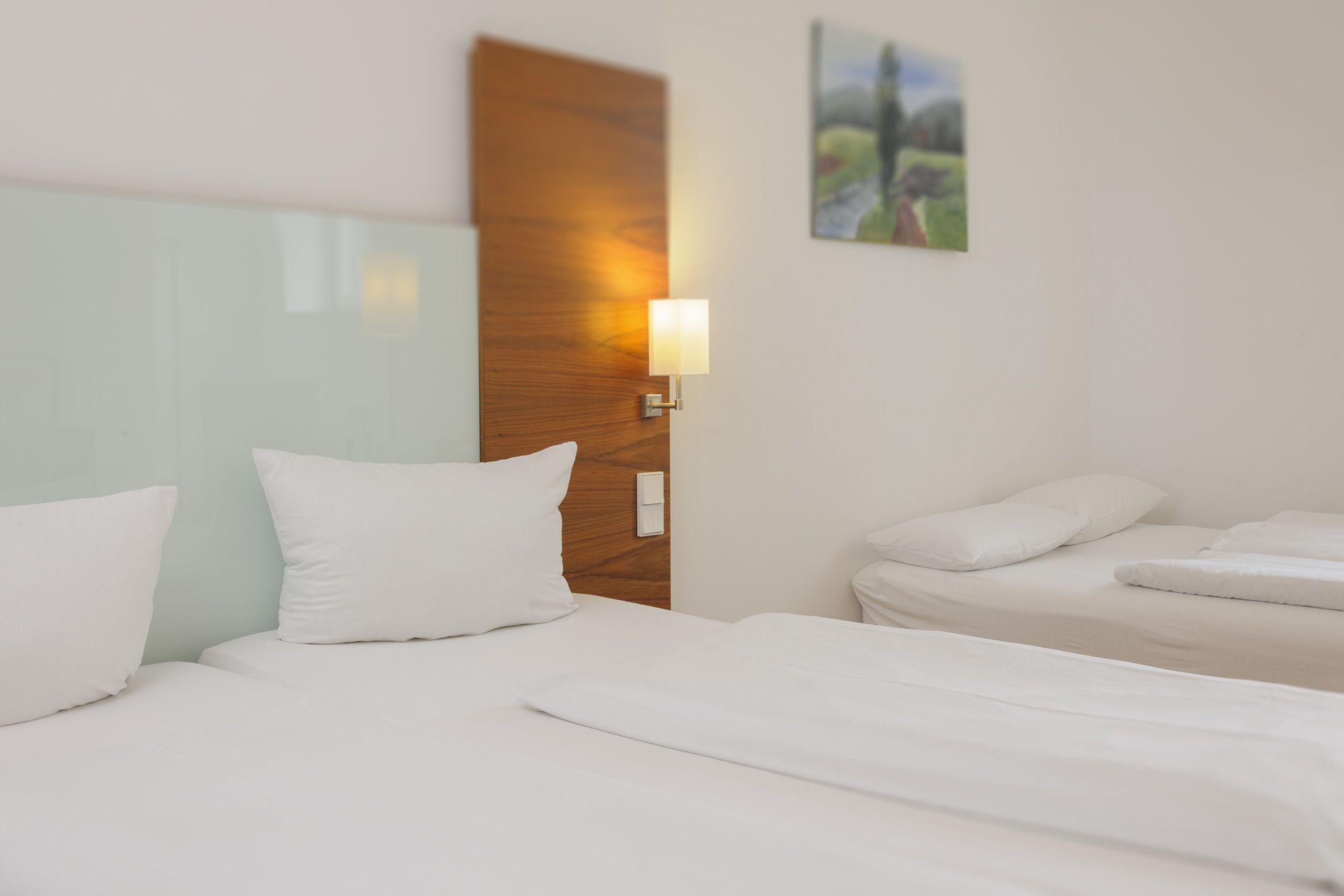 A hotel room with a wooden headboard, a bedside lamp, and a painting on the wall.