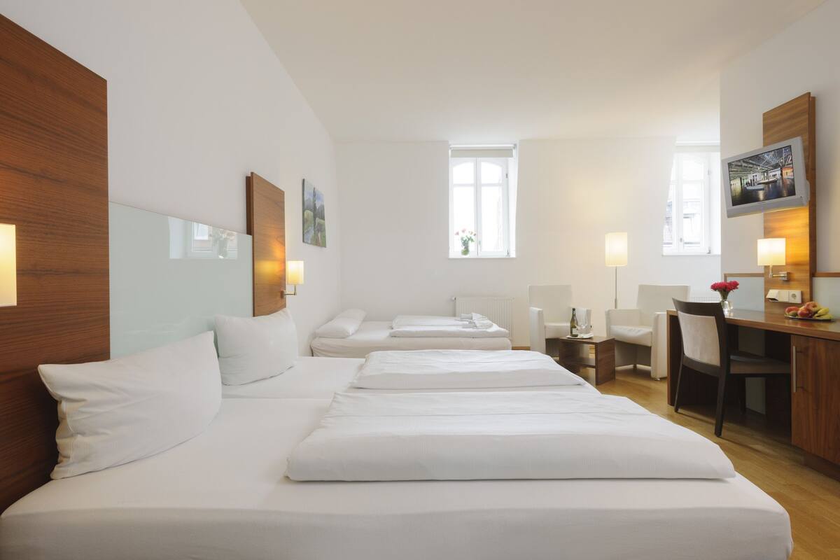 A hotel room with a large bed, a desk, a chair, and a TV.