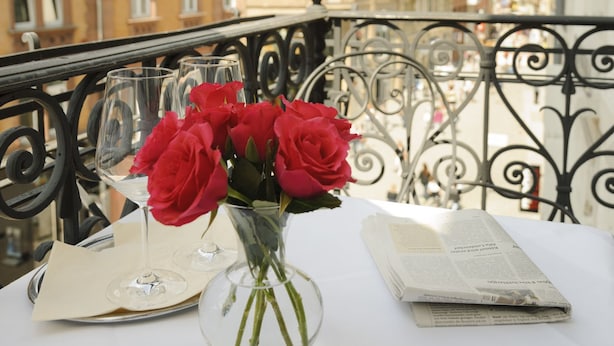 A table with a vase of red roses, two wine glasses, and a menu on a balcony overlooking historic buildings. - Hotel Augustiner Tor (Konstanz)