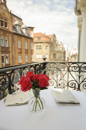 A table with a vase of red roses, two wine glasses, and a menu on a balcony overlooking historic buildings. - Hotel Augustiner Tor (Konstanz)