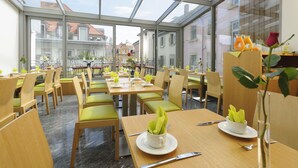 A restaurant with a glass roof, wooden tables, and green chairs. - Hotel Augustiner Tor (Konstanz)