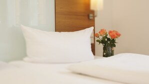 A neatly made bed with white bedding and a single white pillow. - Hotel Augustiner Tor (Konstanz)