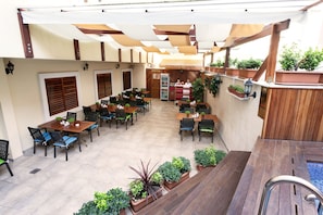 Un café avec terrasse, doté de tables et de chaises en bois, de plantes en pot et d’une plateforme en bois.