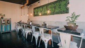 A dining area with white chairs, a long table, and hanging light bulbs. - Trash Deluxe (Maastricht)