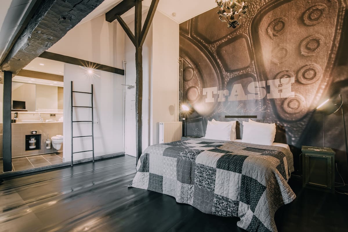 A modern bedroom with a large bed, a quilted headboard, and a view of a kitchen and bathroom through an open door.