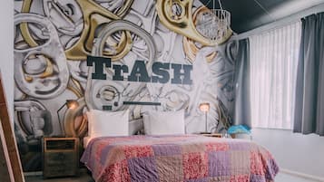 A bedroom with a bed, a wall mural, a hanging light fixture, and a red barrel.