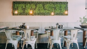 A restaurant interior with white metal chairs, a green wall with hanging lights, and a black tiled floor. - Trash Deluxe (Maastricht)