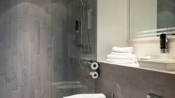 Un baño moderno con ducha envuelta en vidrio, inodoro y lavamanos con espejo superior.