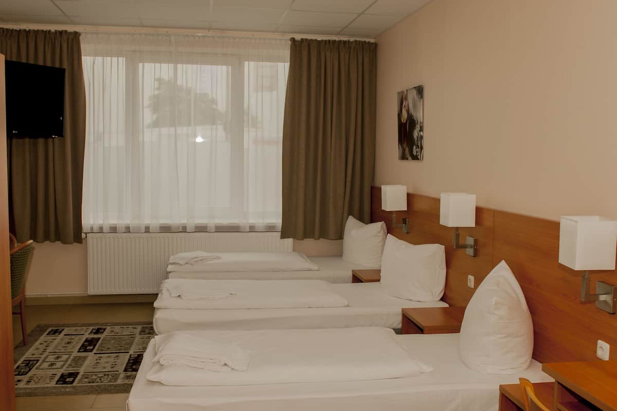 Une chambre d’hôtel avec trois lits simples, une télévision, un radiateur et une fenêtre avec des rideaux.