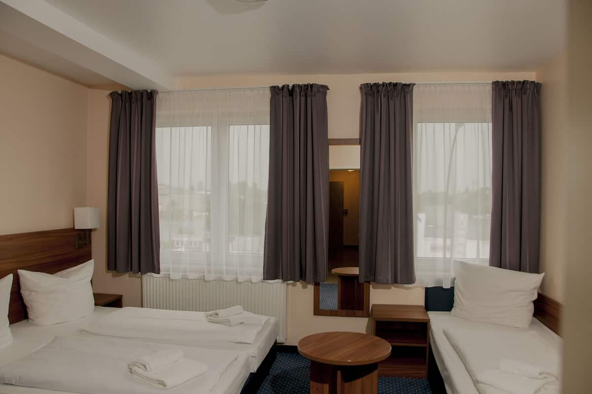 Une chambre d’hôtel avec deux lits, une petite table ronde, un miroir et une fenêtre avec des rideaux.