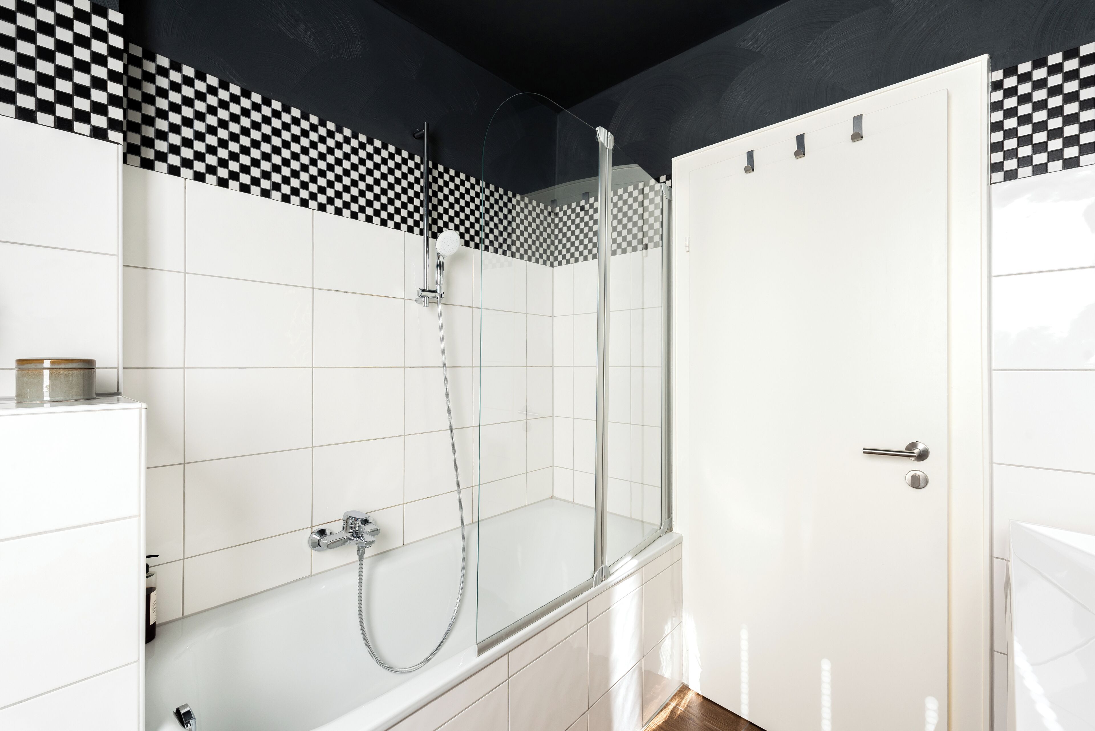 A modern bathroom with a checkered wall pattern, a glass shower enclosure, and a white door.