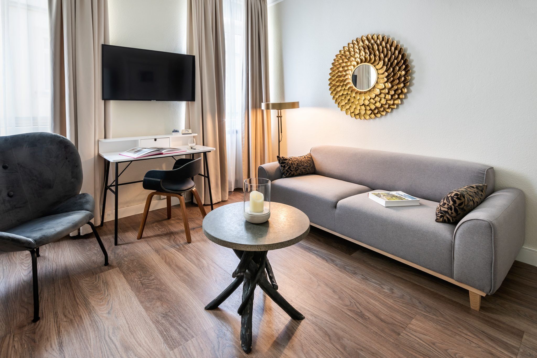 Una sala de estar moderna con un sofá gris, una mesa redonda con una vela, un televisor de pantalla plana y un adorno en la pared.