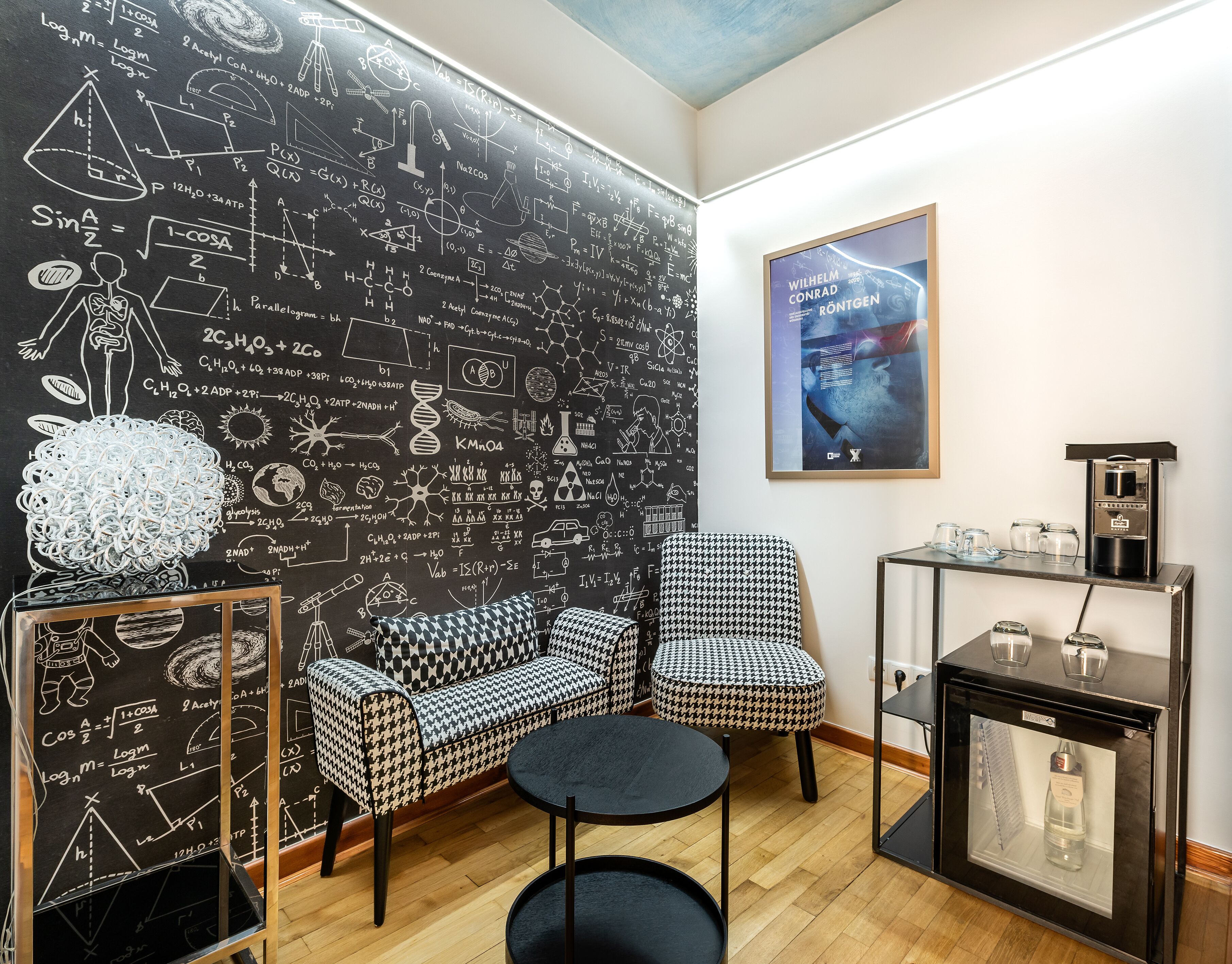 A modern room with a blackboard filled with scientific equations and diagrams, a houndstooth patterned sofa, a round black table, and a coffee machine.