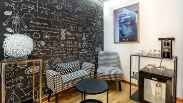 A modern room with a blackboard filled with scientific equations and diagrams, a houndstooth patterned sofa, a round black table, and a coffee machine.