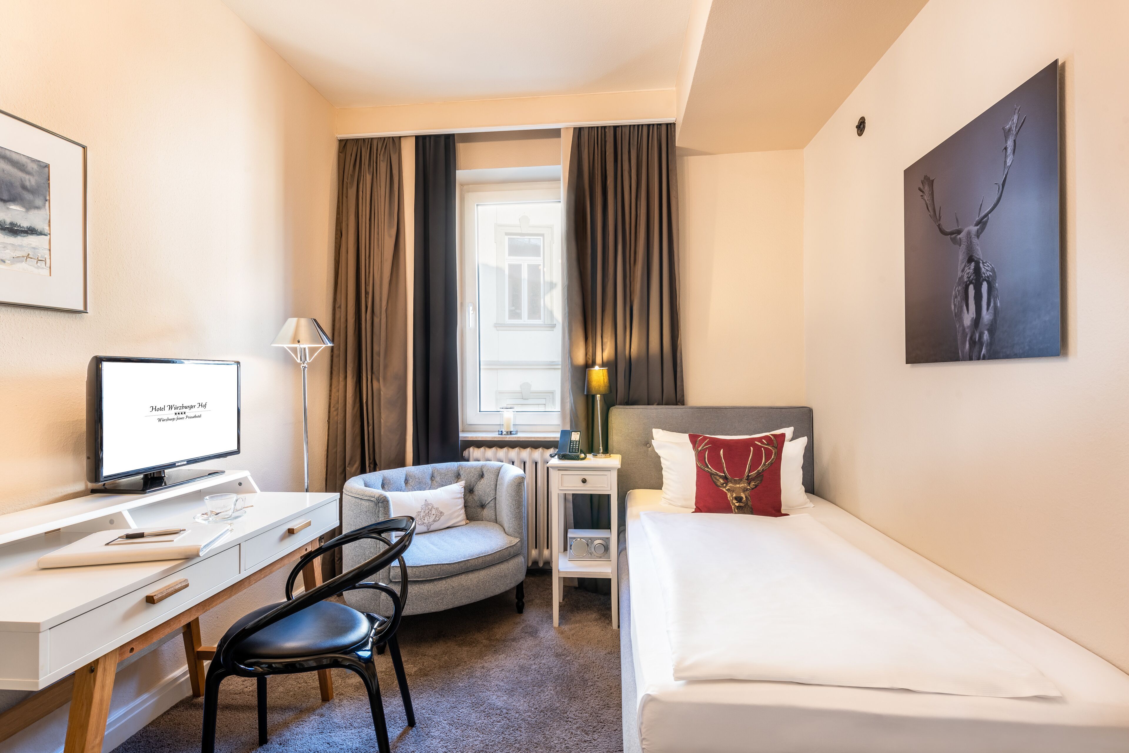 Una habitación de hotel con cama, escritorio, silla y monitor de computadora.