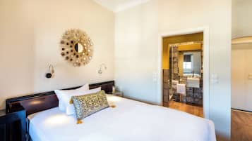 Habitación de hotel con una cama grande, un espejo decorativo, una mesita de noche y un baño visible a través de una puerta abierta.