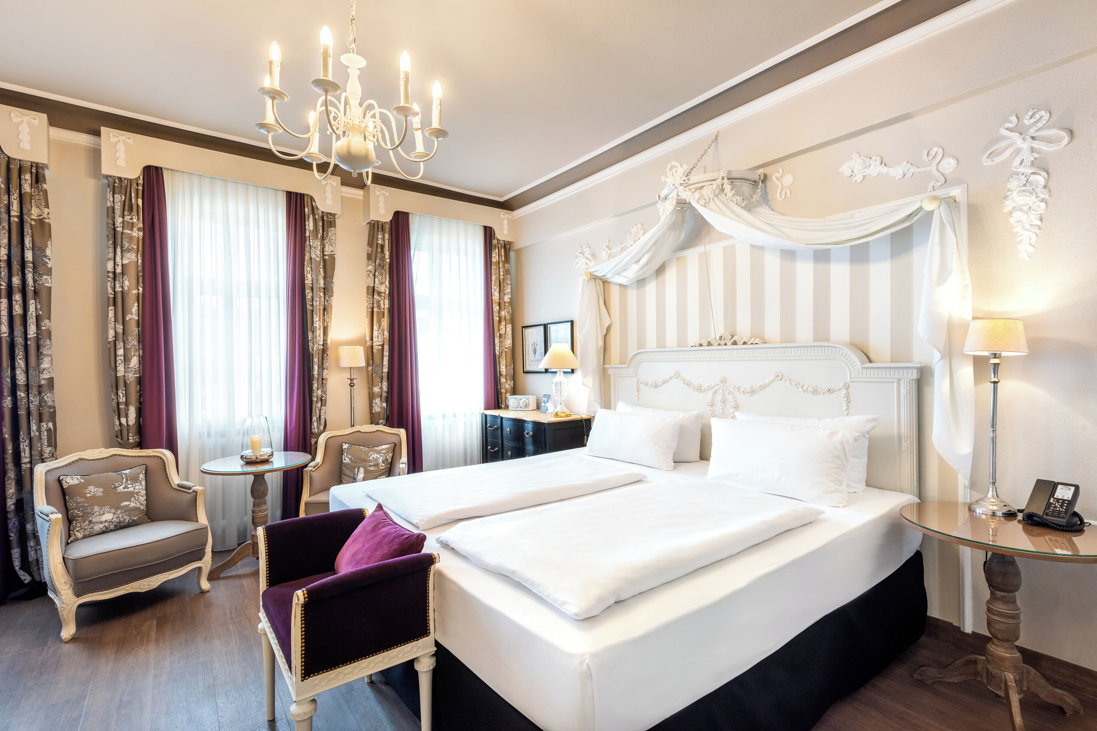 Une chambre d’hôtel avec un grand lit, un lustre, une coiffeuse avec un miroir et une petite table avec une lampe.