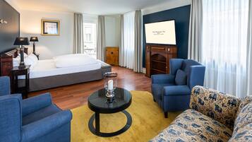A hotel room with a bed, two armchairs, a sofa, a coffee table, a TV, and a wooden cabinet.