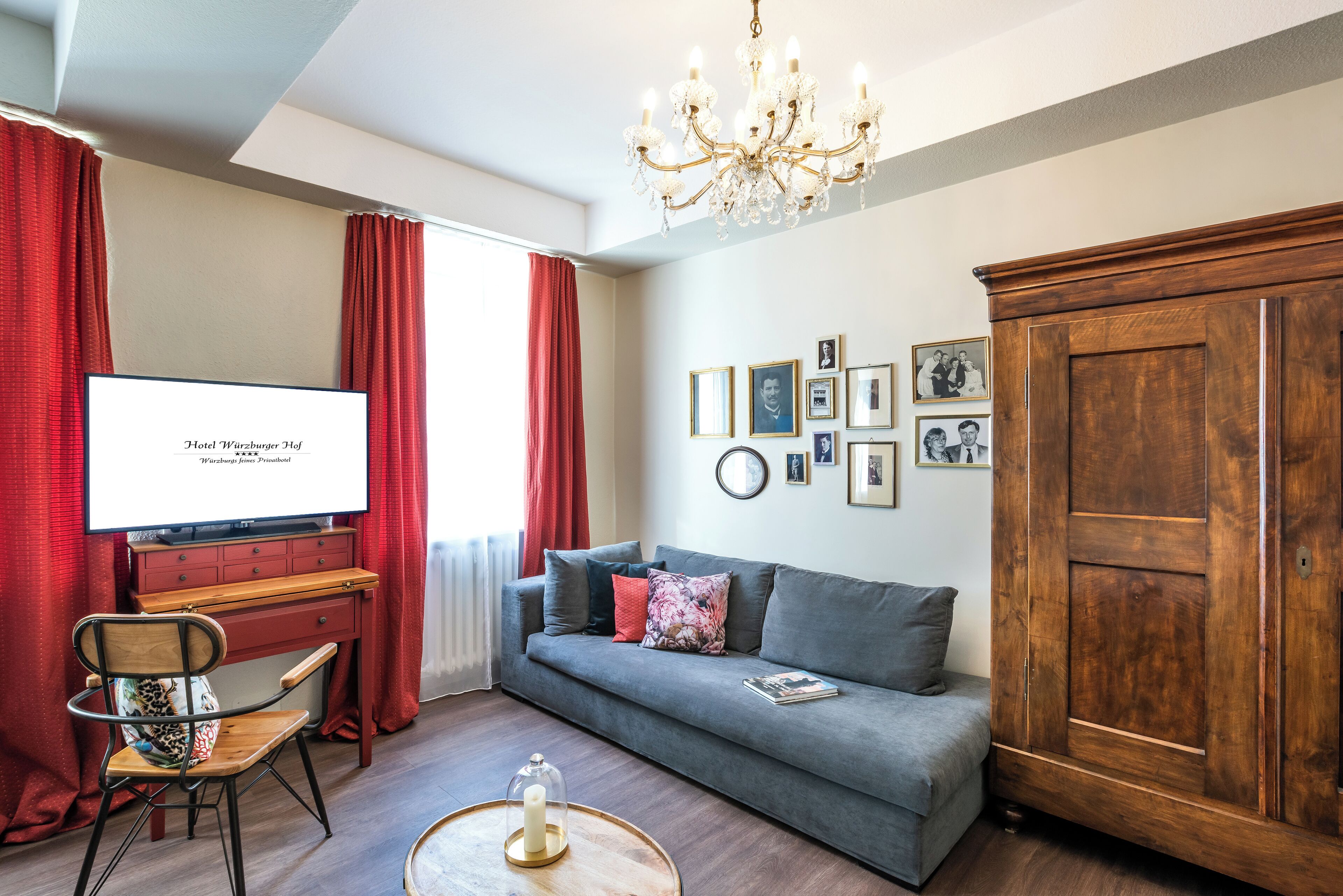 A living room with a grey sofa, a wooden cabinet, a TV, and a chandelier.