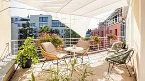 A balcony with outdoor seating, potted plants, and a view of buildings. - Hotel Würzburger Hof (Würzburg)