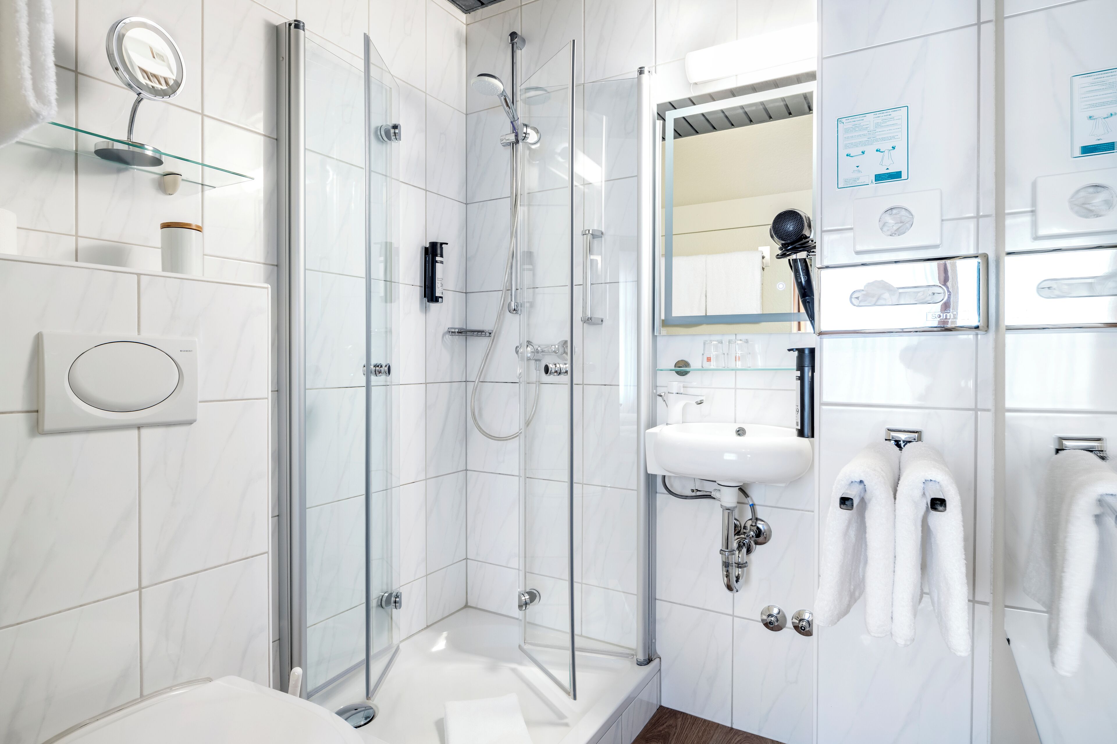 Un baño moderno con ducha de vidrio, un lavamanos blanco y un espejo con luz integrada.