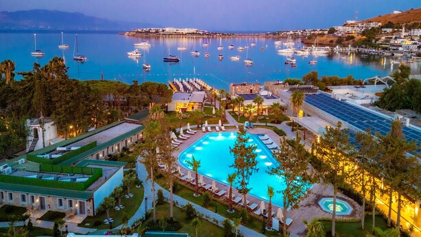 Un complejo turístico con piscina, tumbonas y vistas al puerto deportivo con barcos.