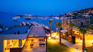 Un puerto deportivo con barcos, una zona de piscina con sombrillas y sillas, y vistas al pueblo.