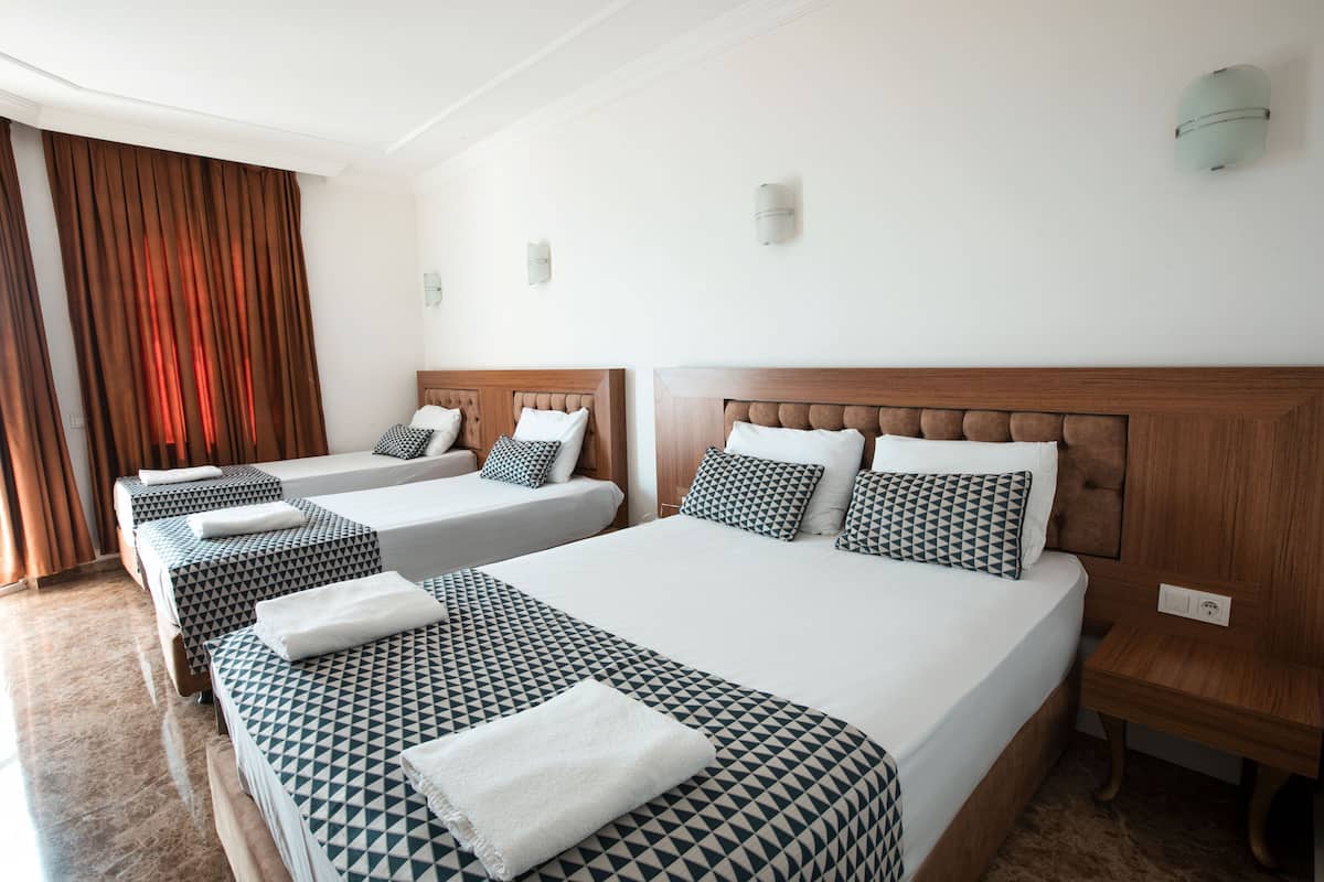 A hotel room with three beds, each with patterned bedding and pillows. There are bedside tables and a nightstand with a lamp.