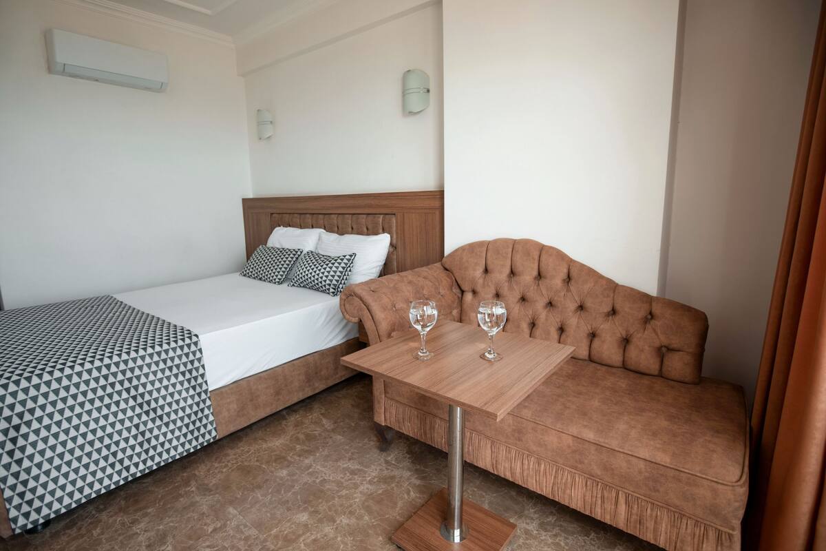 A hotel room with a bed, a sofa, and a small table with two glasses on it.
