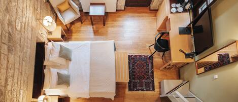 Una habitación con cama, escritorio, silla, mesita, lámpara, televisor y una escalera.