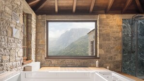 Un baño con paredes de piedra, un ventanal grande, una bañera y una zona de ducha.