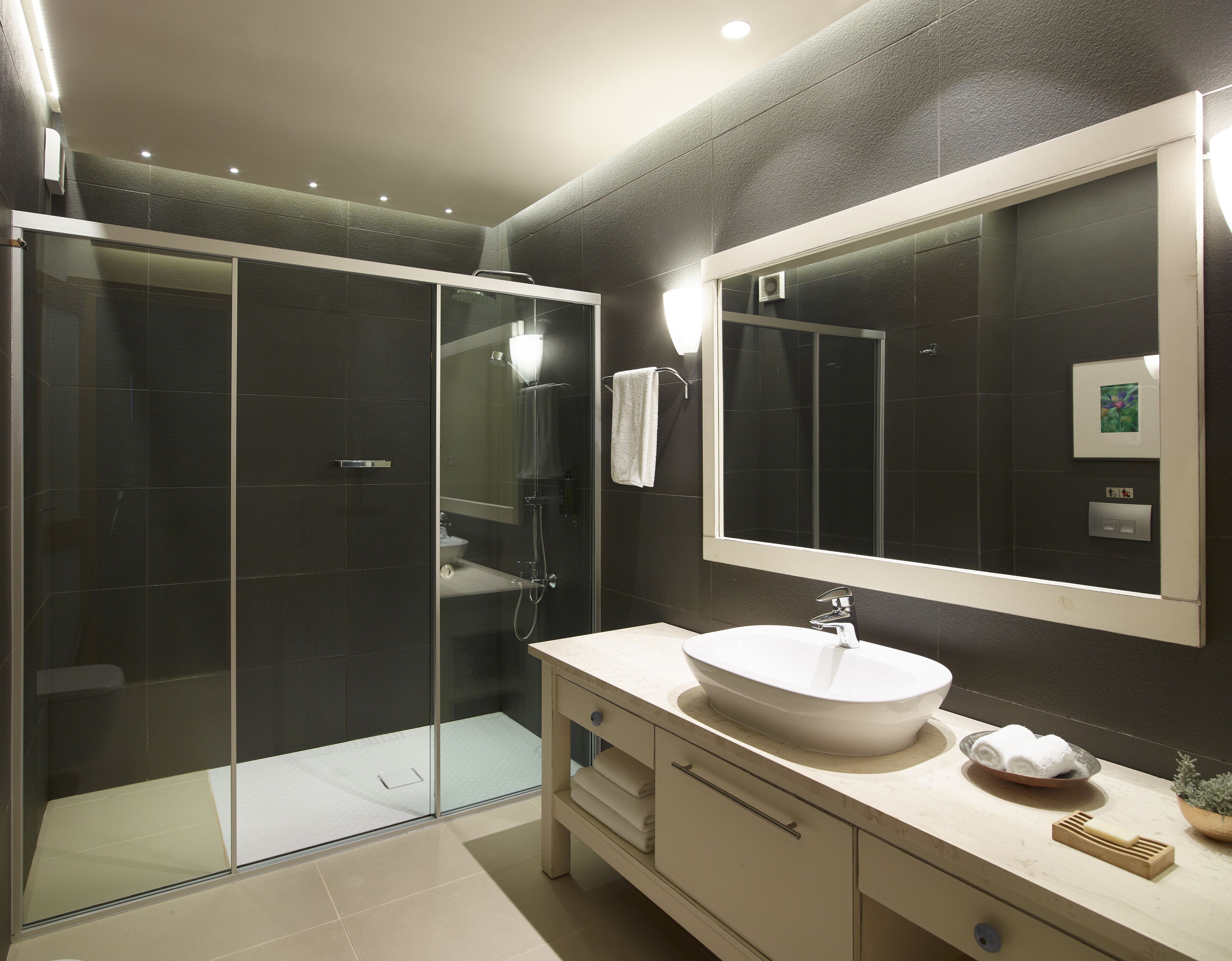 A modern bathroom with a glass-enclosed shower, a large mirror, and a white sink.