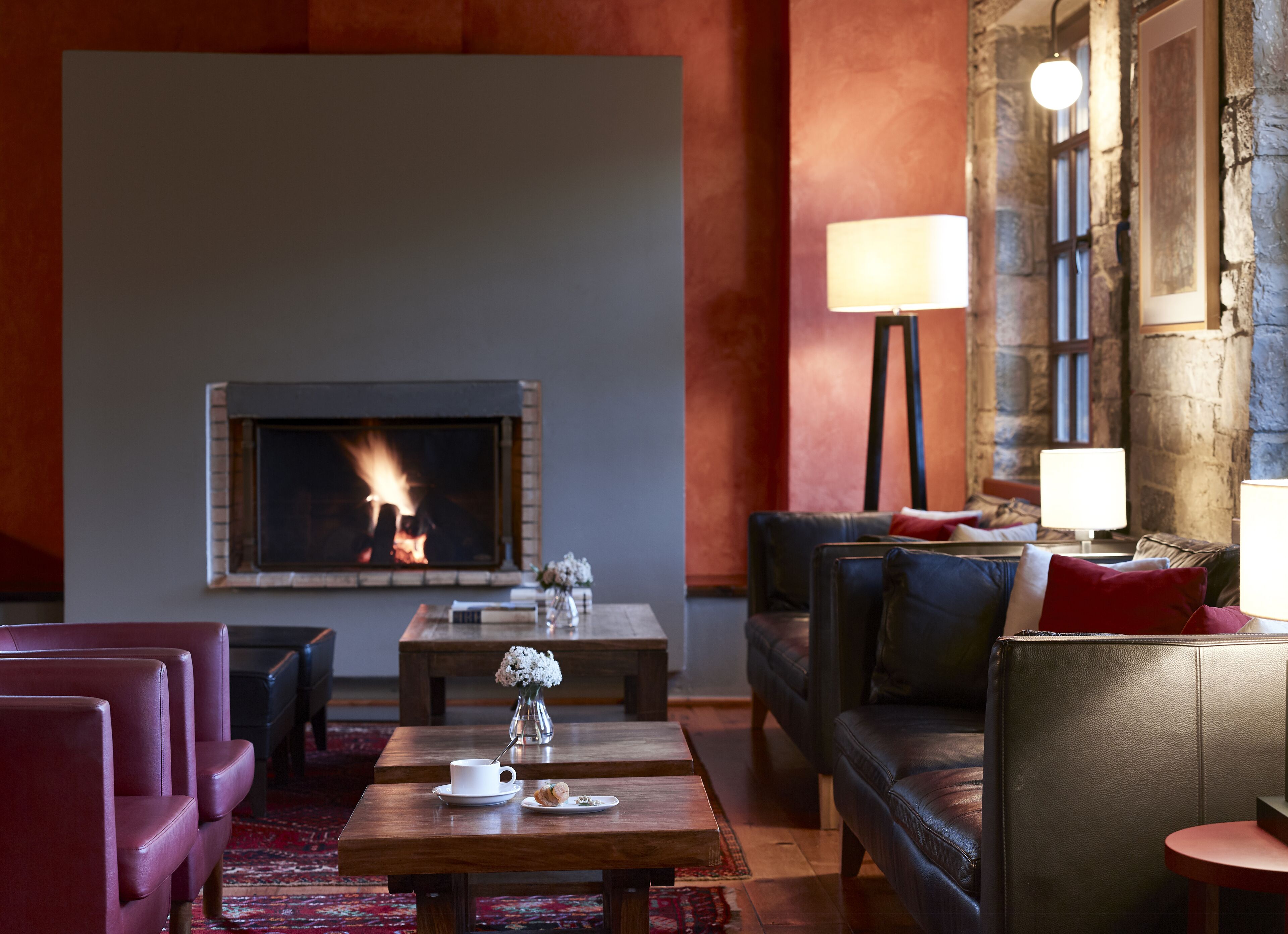 A cozy living room with a fireplace, leather sofas, a coffee table, and a lamp.