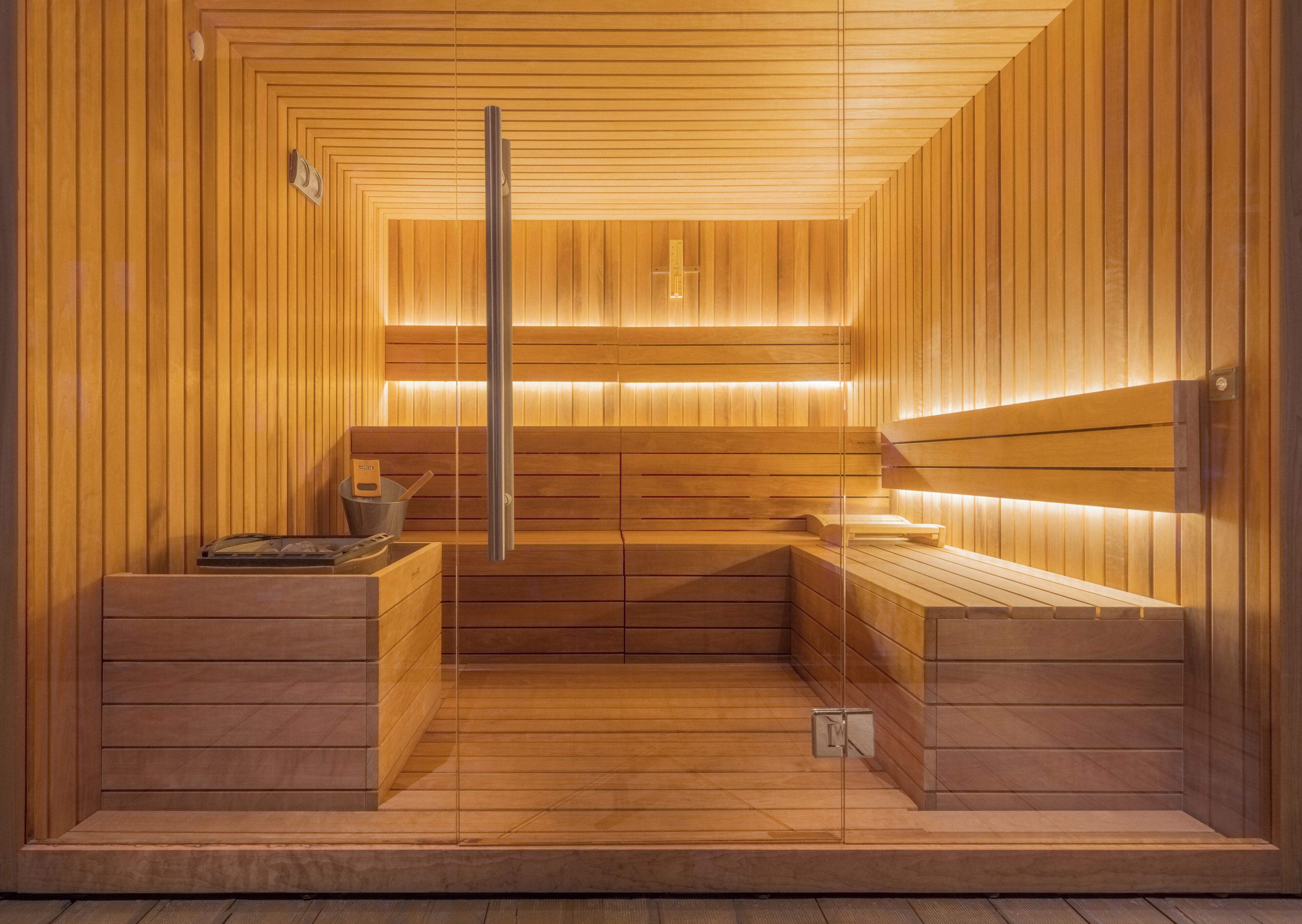 A sauna with wooden walls and benches, a glass door, and a towel rack.